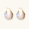 Shell-shaped hoop earrings with iridescent blue-pink enamel and gold trim on cream background