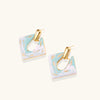 Geometric square enamel earrings with marbled turquoise and lavender pattern, gold U-shaped connector on cream background.