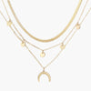 Four-layer gold necklace with herringbone chain, disc charms, and crescent moon pendant on cream background
