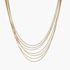 Seven delicate gold-plated snake chains create an elegant layered necklace on a neutral background.