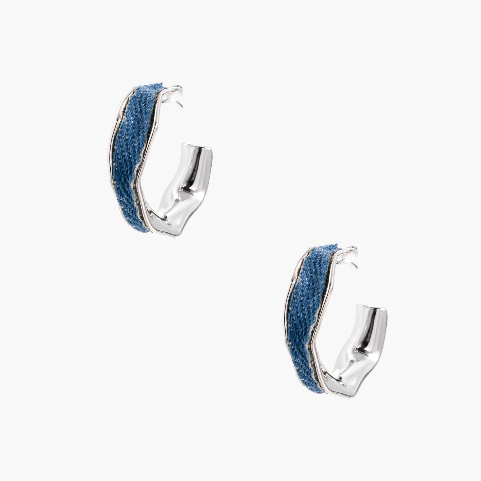 Silver huggie hoops with blue denim fabric inlay strip and polished white gold plated finish on cream background.
