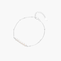 Delicate rhodium-plated silver chain bracelet with row of small baroque pearls centered on white background.